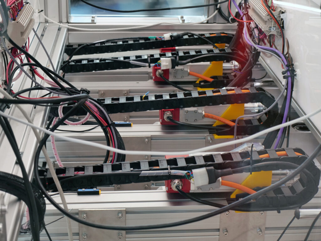 Vista ravvicinata dei motori e dei componenti elettronici di un calcetto robotizzato. Sono visibili diversi cavi colorati, guide di plastica nera per il cablaggio e connettori metallici, montati su strutture in metallo.
